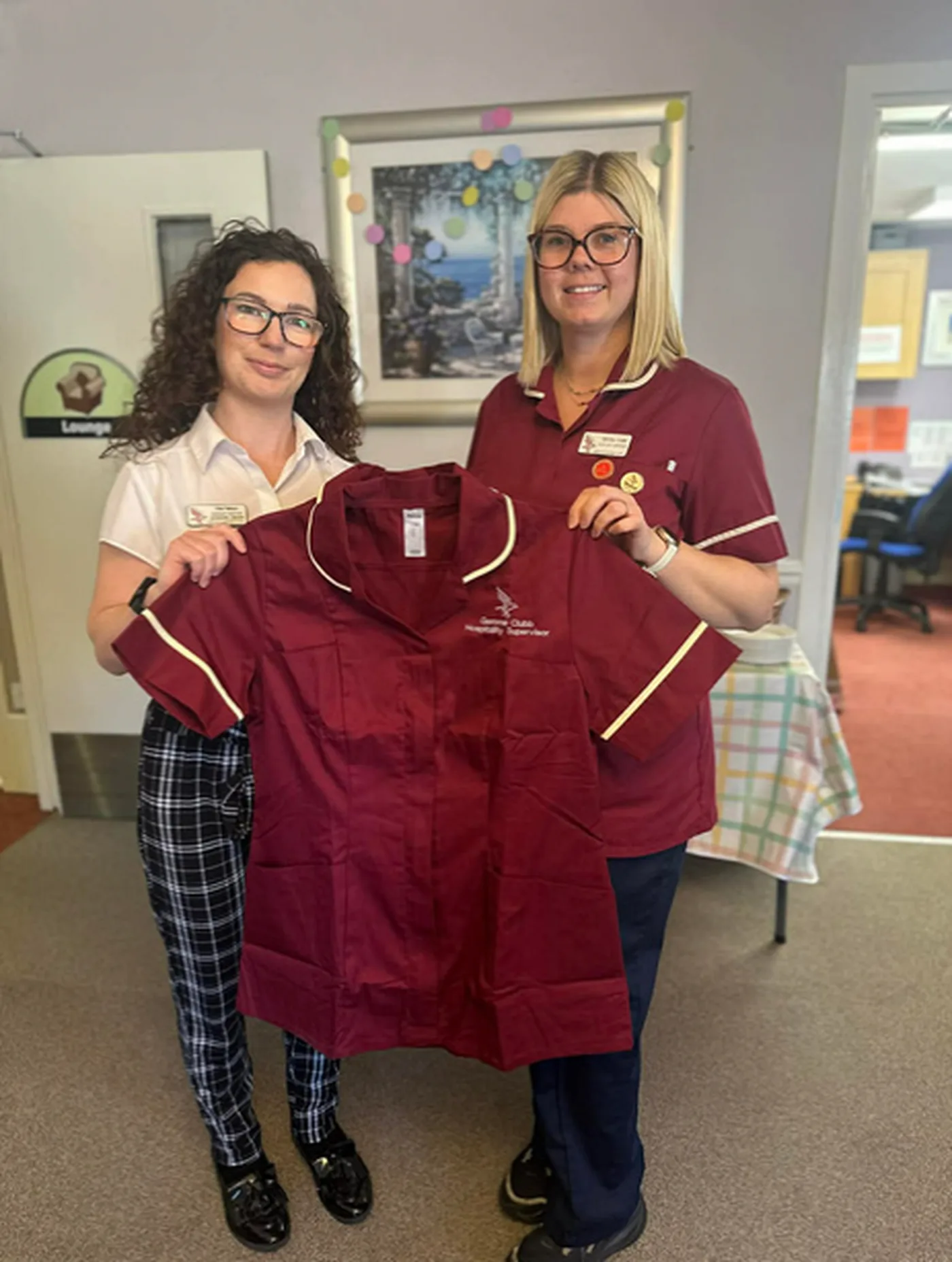 Chloe Pattisson, Hospitality Facilitator at Meallmore, on the left, holding a Meallmore housekeeping uniform with a colleague in a care home