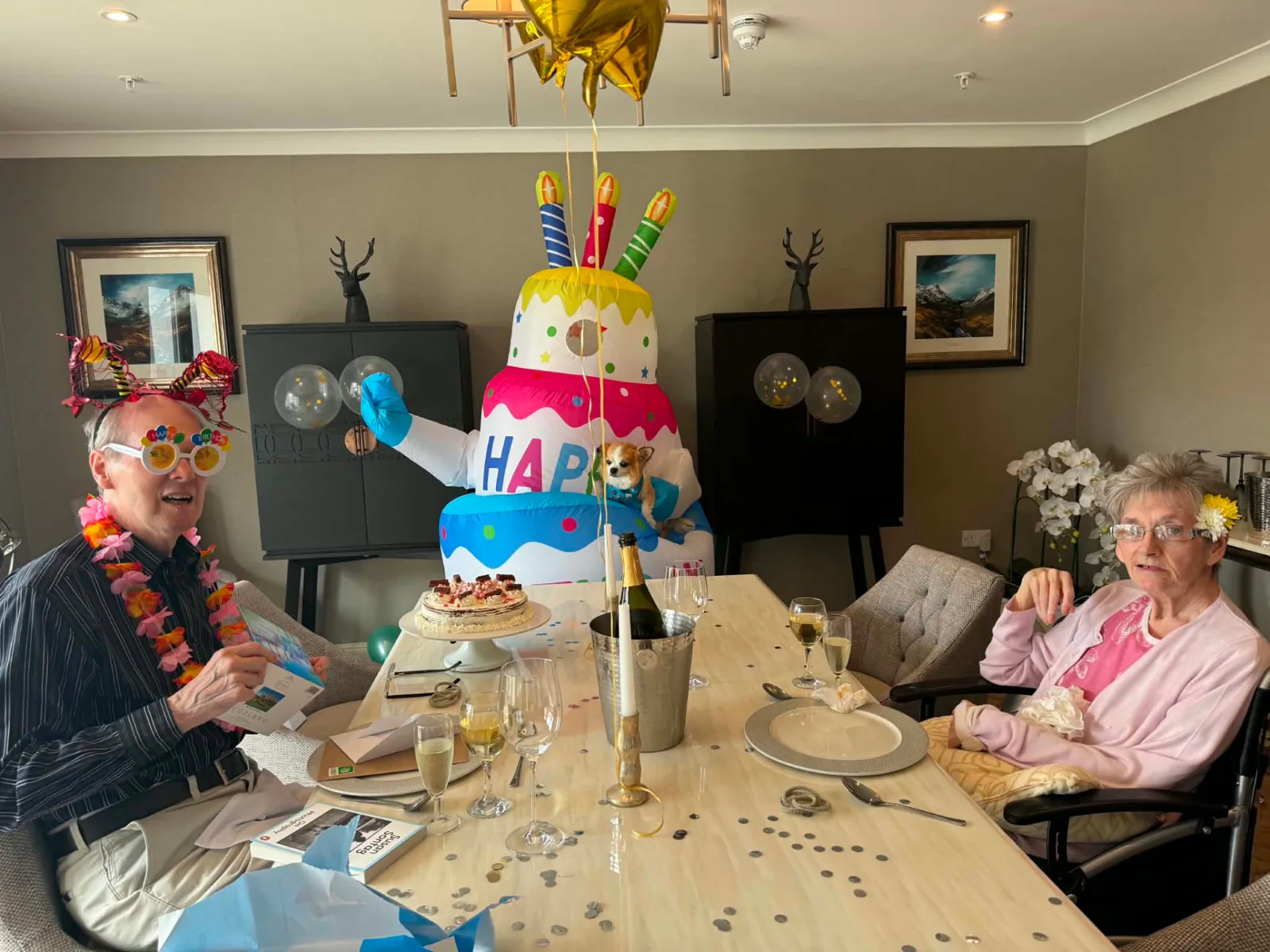 Andy and Mary Wilson celebrating with cake, balloons and champagne in the fine dining room at Greenan Manor