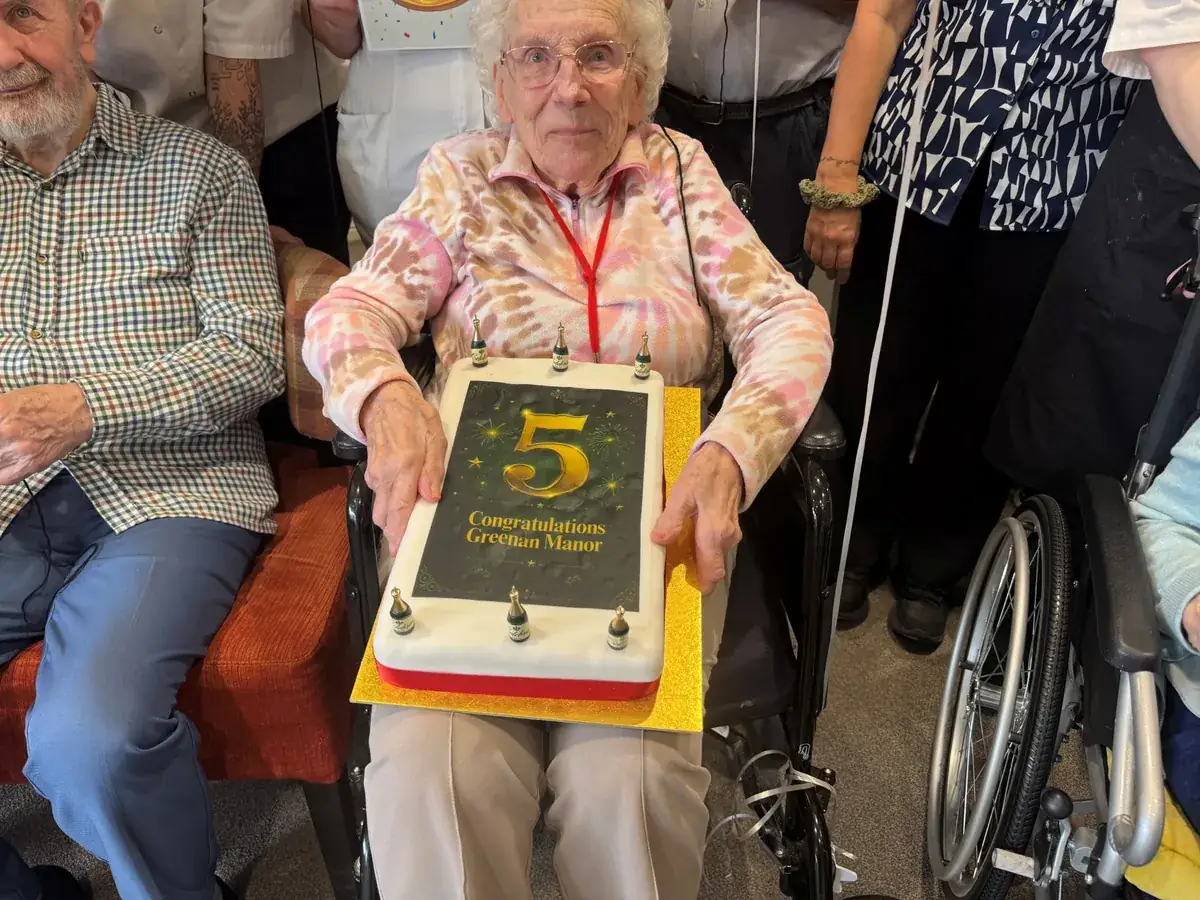 A Greenan Manor resident holding a celebration cake decorated with a gold number five