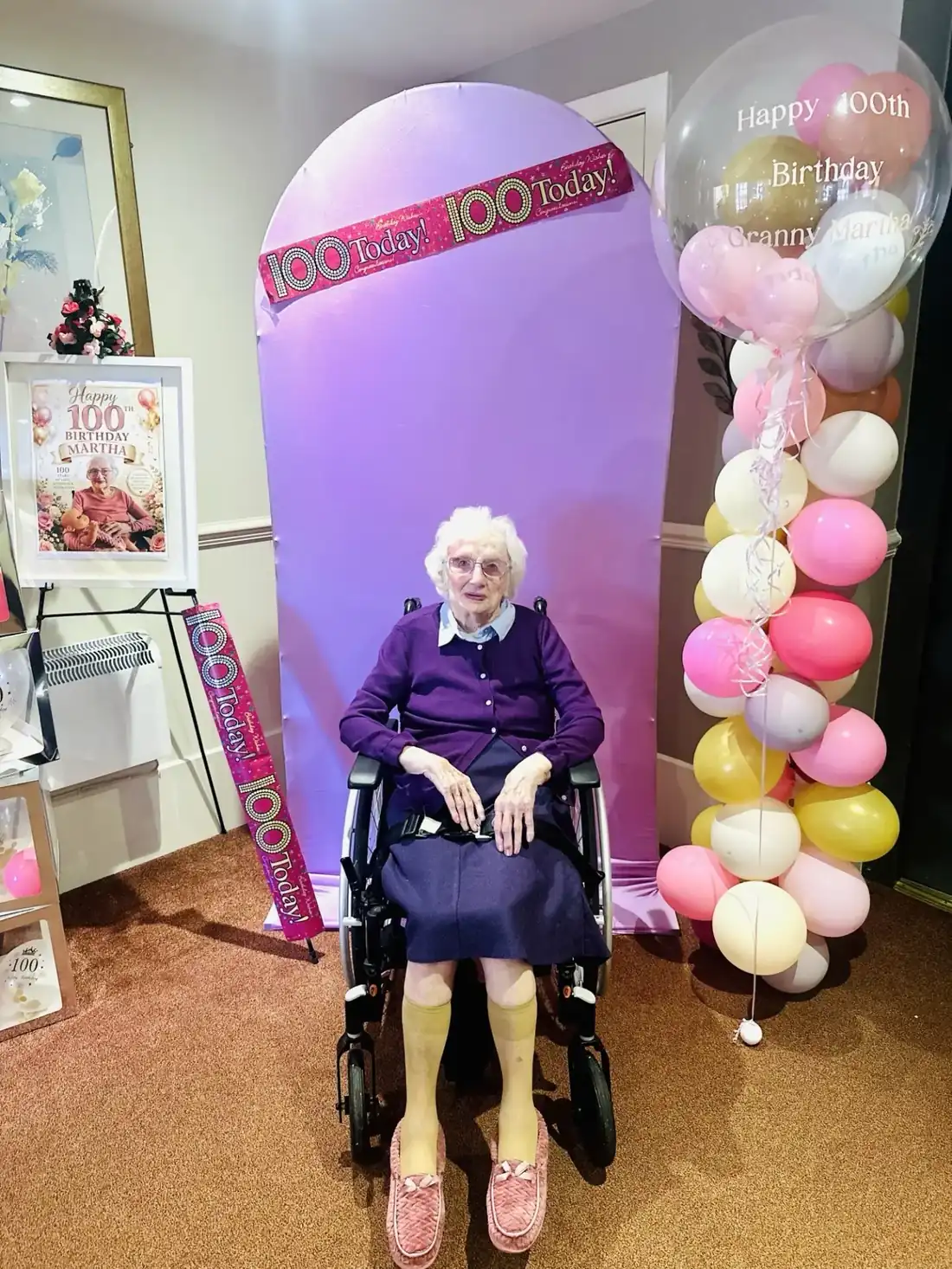 Martha, a resident at Kynnaird House Care Home, sitting in front of a 100 Today birthday backdrop with balloons