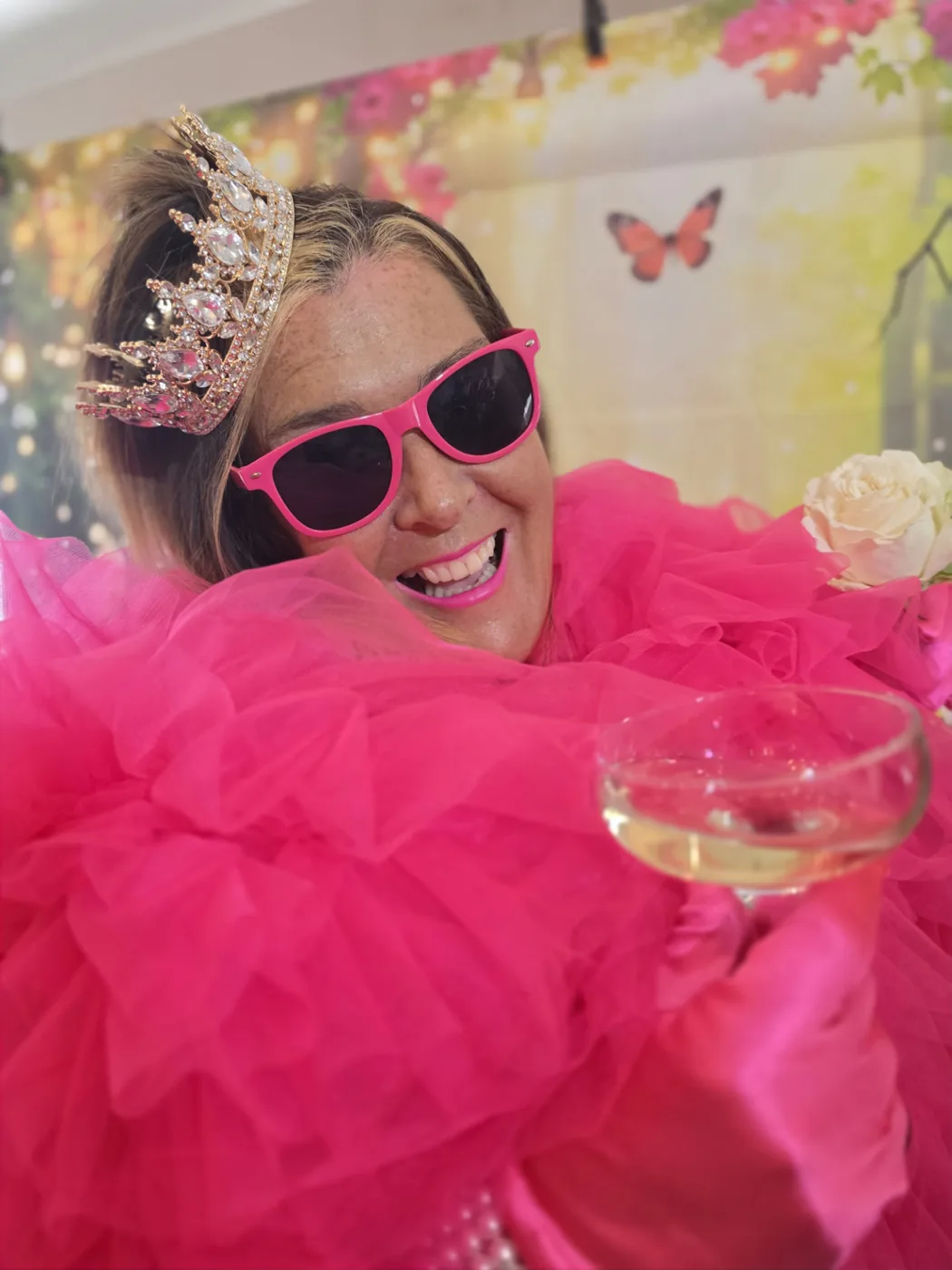 A member of the Parklands Care Home Glam Squad in a pink gown, crown and sunglasses raising a glass during the photoshoot