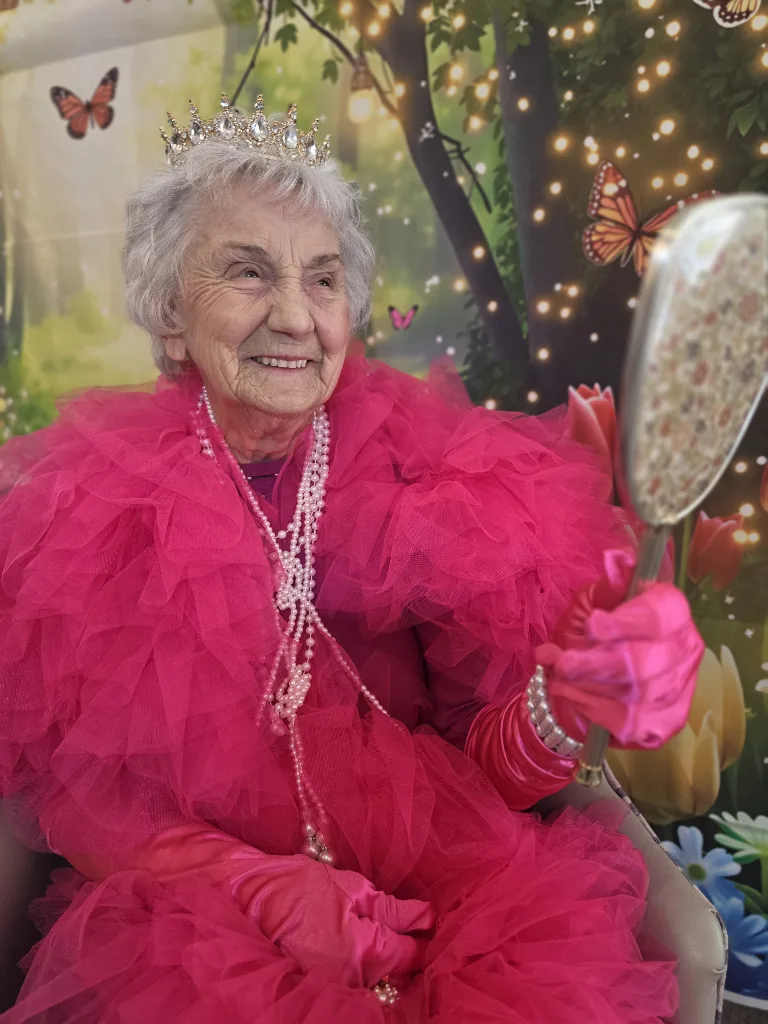 A resident at Parklands Care Home holding a hand mirror while wearing a crown, pearls and a pink gown