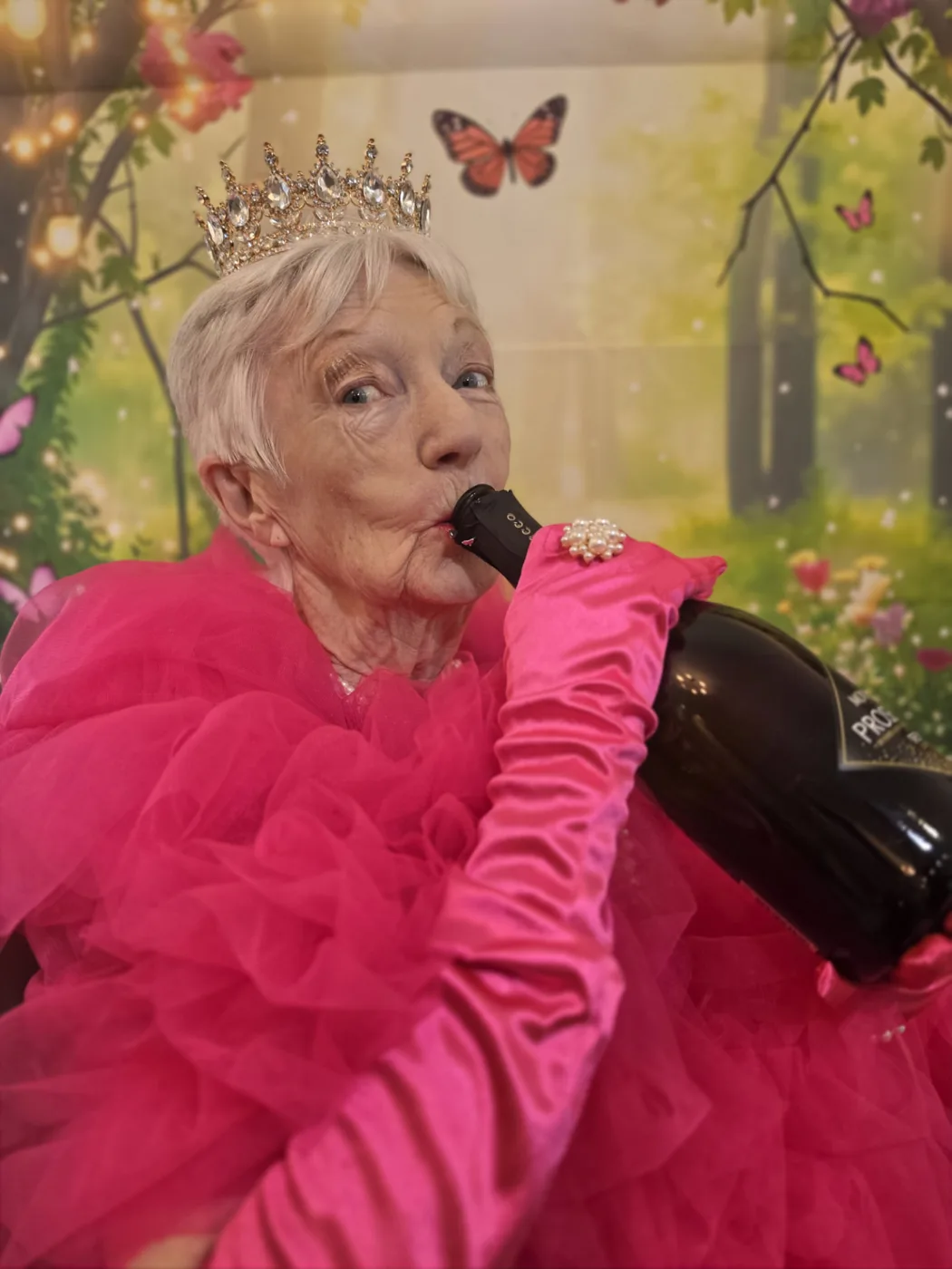 A resident at Parklands Care Home in a crown, pink gown and satin gloves holding a bottle during the Queen for the Day photoshoot