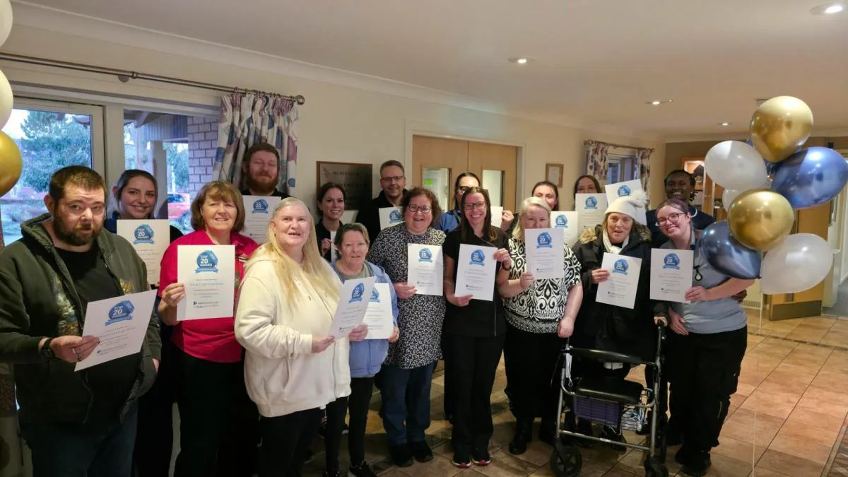 Residents and colleagues at Hilton Court care home in Rosyth holding Top 20 Care Home award certificates beside gold and blue balloons