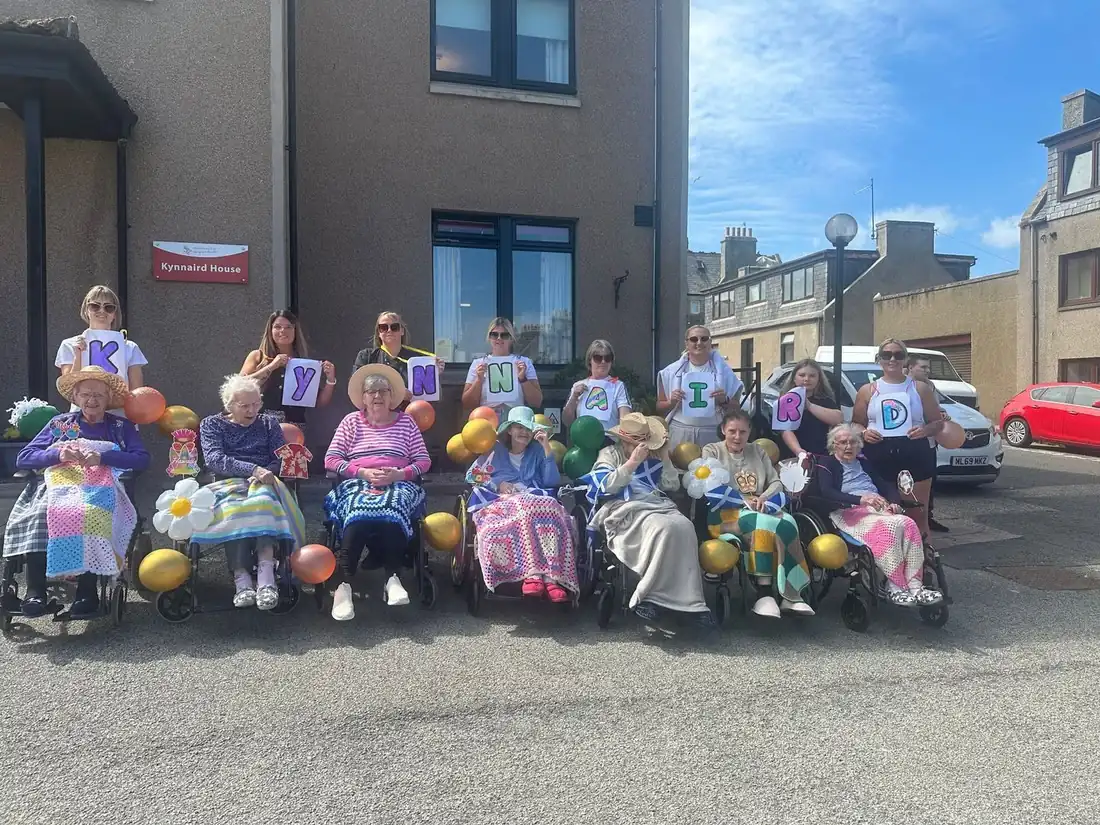 Residents and colleagues outside Kynnaird House care home in Fraserburgh holding letters spelling KYNNAIRD on a sunny day