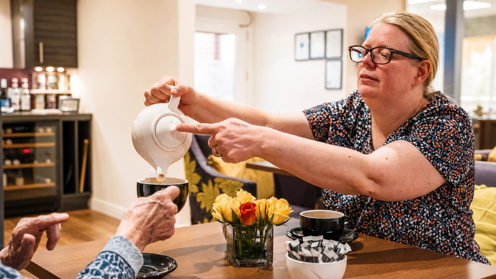 A resident being poured a cup of tea beside a vase of fresh flowers at Culduthel Care Home in Inverness
