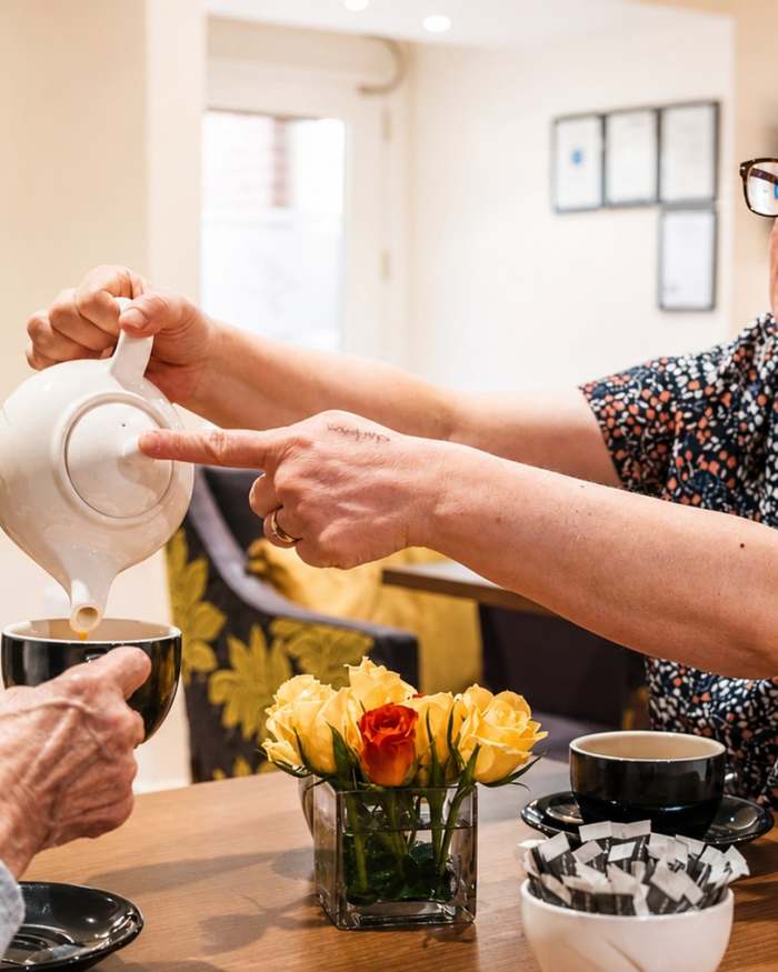 A resident being poured a cup of tea beside a vase of fresh flowers at Culduthel Care Home in Inverness